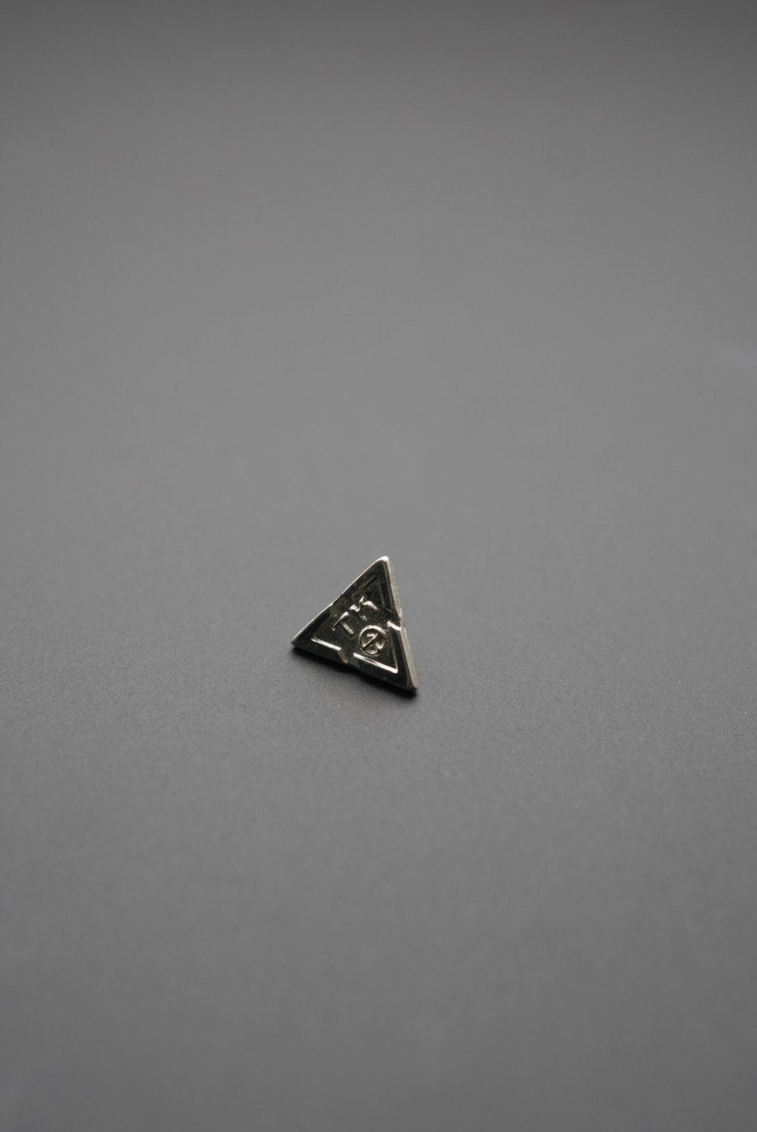 Botón triangular con acabado pulido y diseño técnico