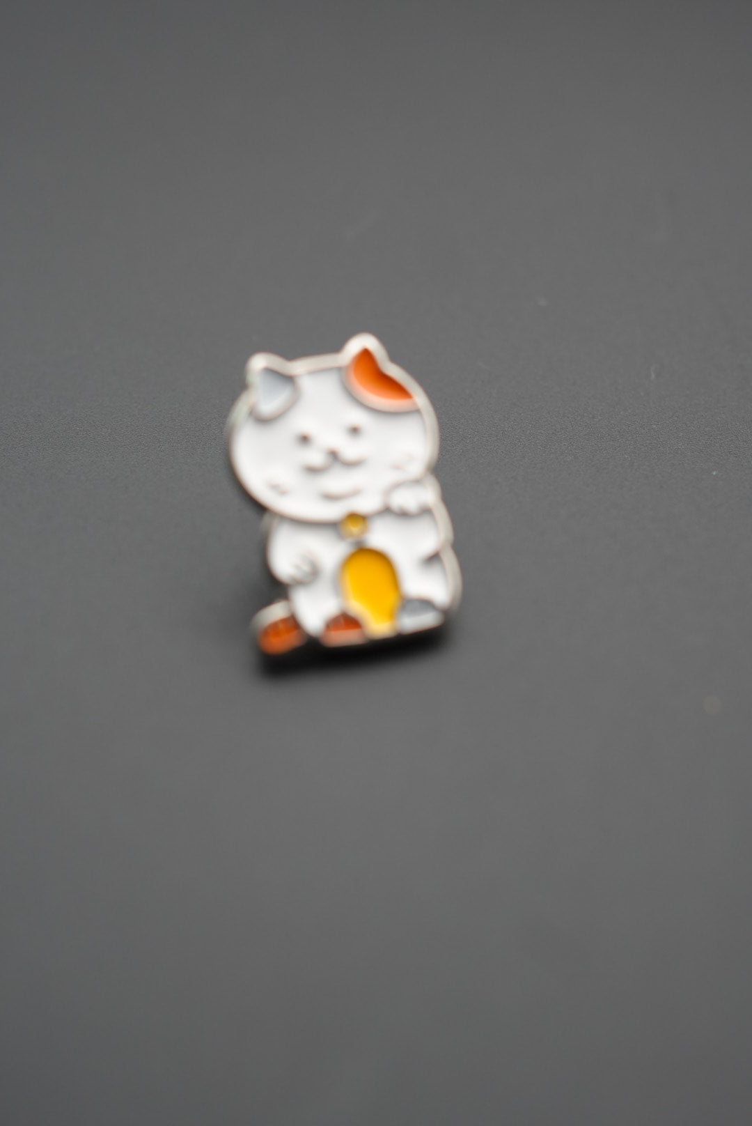 Pin gato Maneki-neko ligeramente desenfocado en fondo gris liso