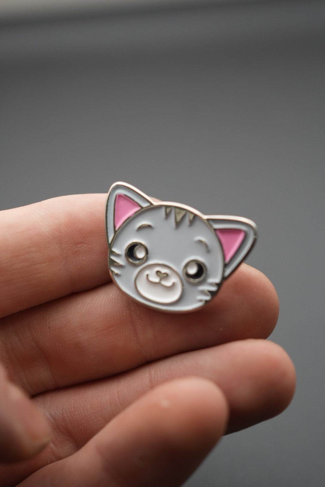Pin con diseño de gato sosteniéndose entre dedos con detalle