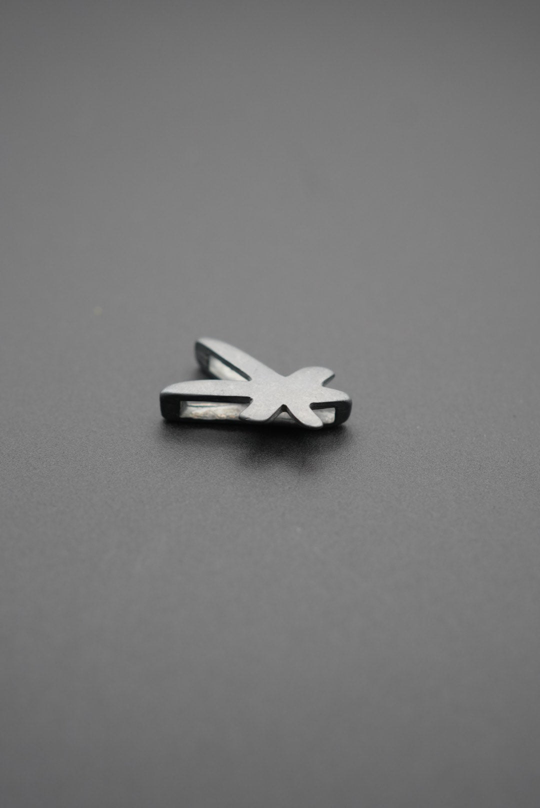 Lado derecho del pin metálico con forma de libélula en fondo gris