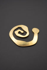 Broche metálico dorado con diseño en espiral colocado sobre superficie gris mate