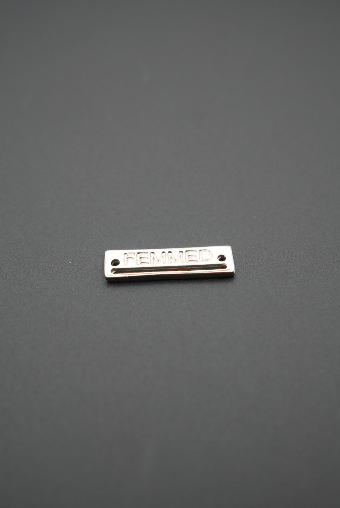 Primer plano de placa metálica FEMMED con acabado brillante sobre fondo gris