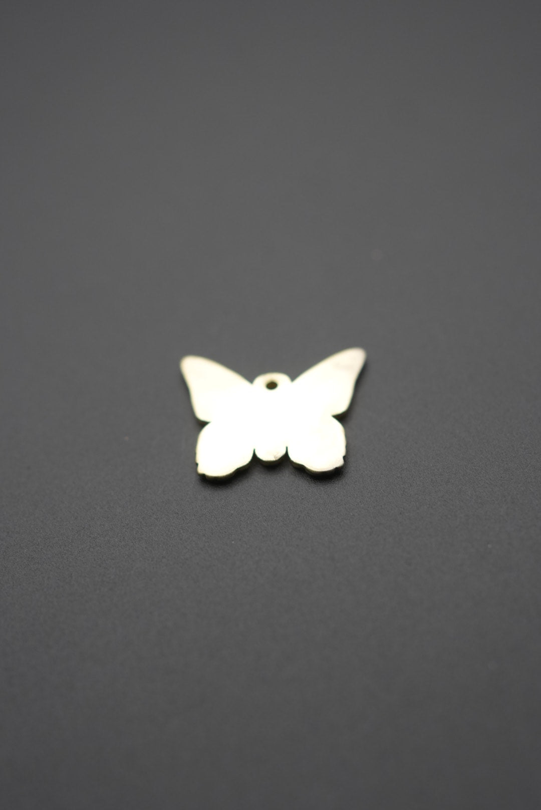 Vista reversa del dije mariposa metálico dorado mostrando superficie lisa