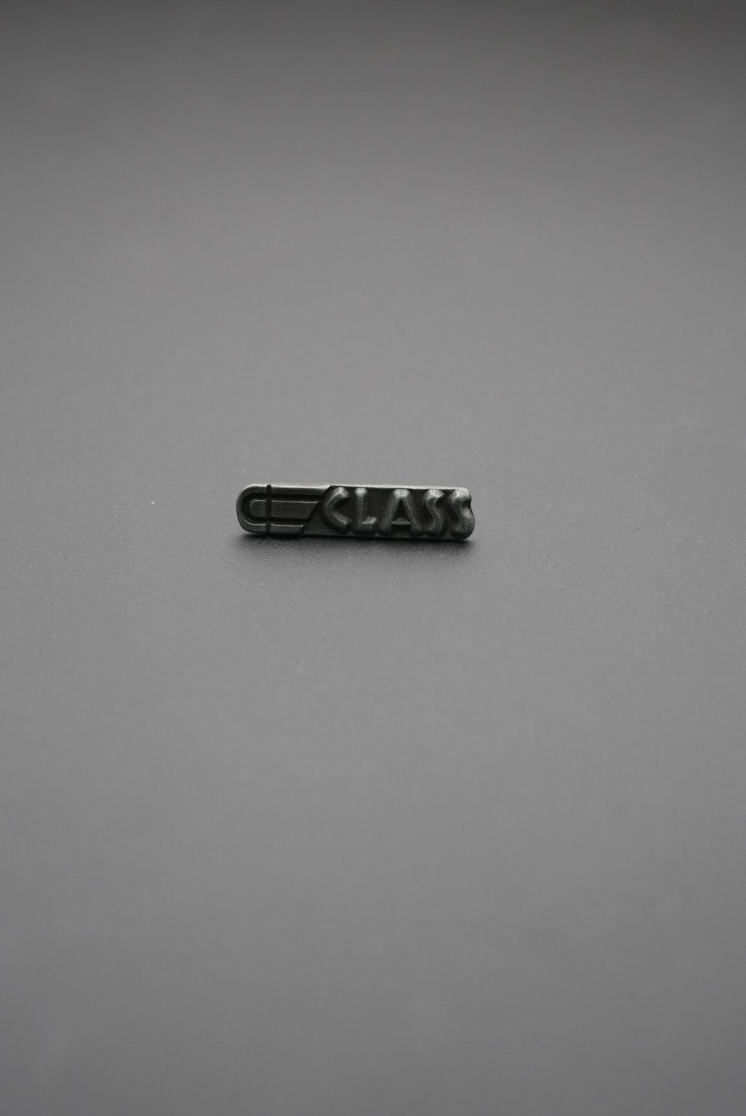 Remache metálico rectangular con grabado CLASS sobre fondo gris