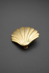 Broche con forma de concha dorada sostenido en una mano