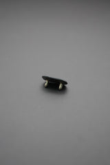 Parte trasera de remache ovalado mostrando doble broche metálico sobre fondo gris