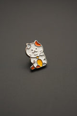 Pin esmaltado gato Maneki-neko con detalles naranjas y amarillos presentado sobre fondo neutral