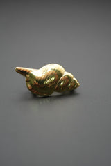 Pin metálico dorado en forma de concha marina sobre fondo gris oscuro vista lateral elevada