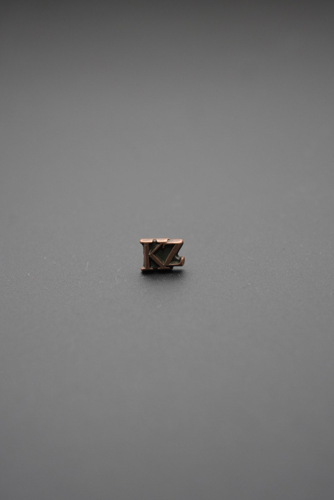 Tachuela metálica triangular con grabado de árboles en color bronce