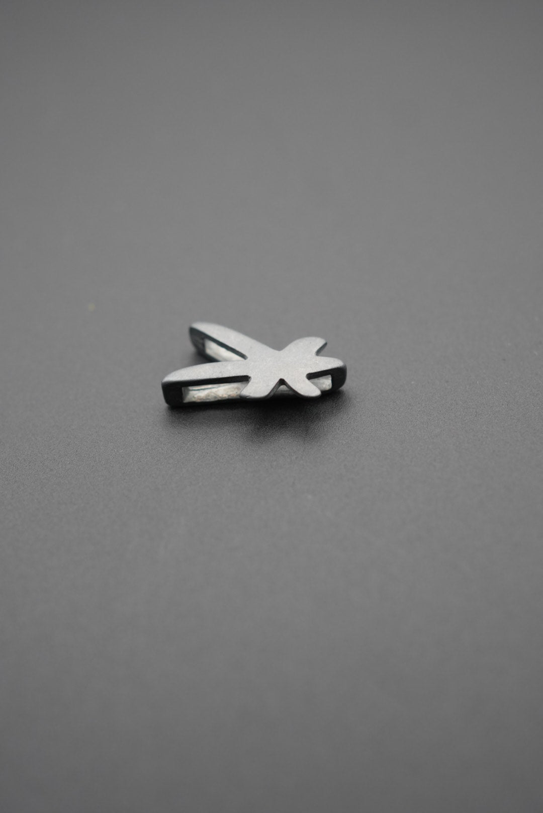 Lado izquierdo del pin metálico con diseño de libélula en fondo gris