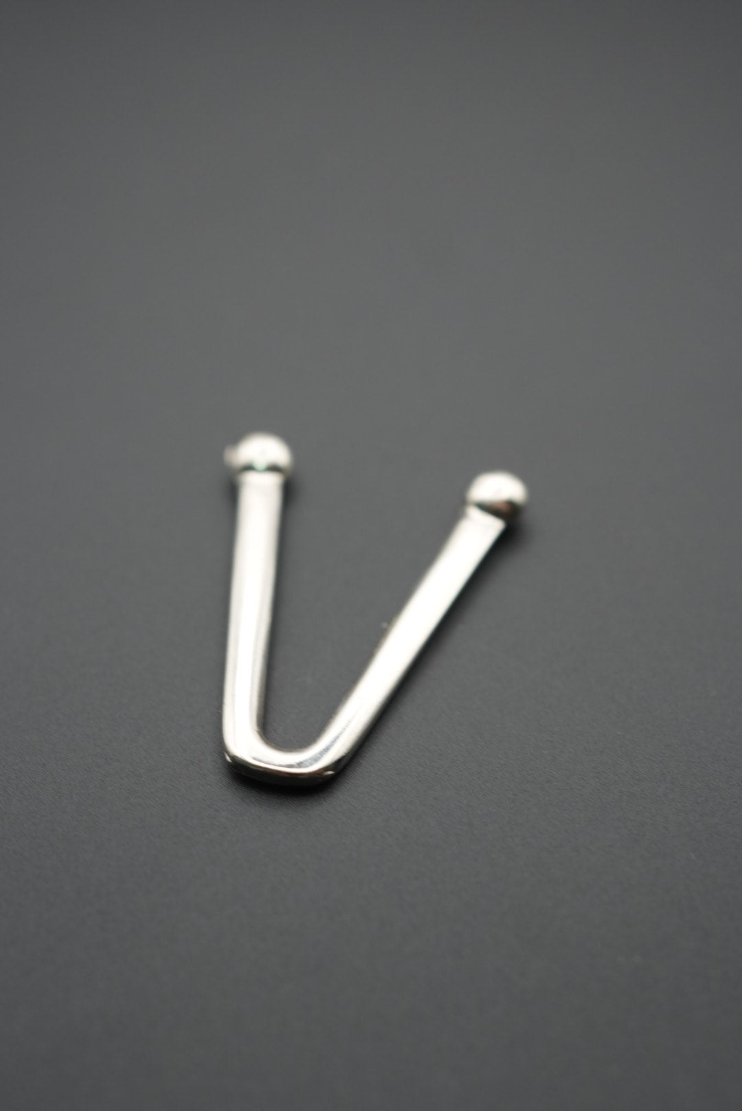 Detalle de gancho metálico en V con fondo neutro gris