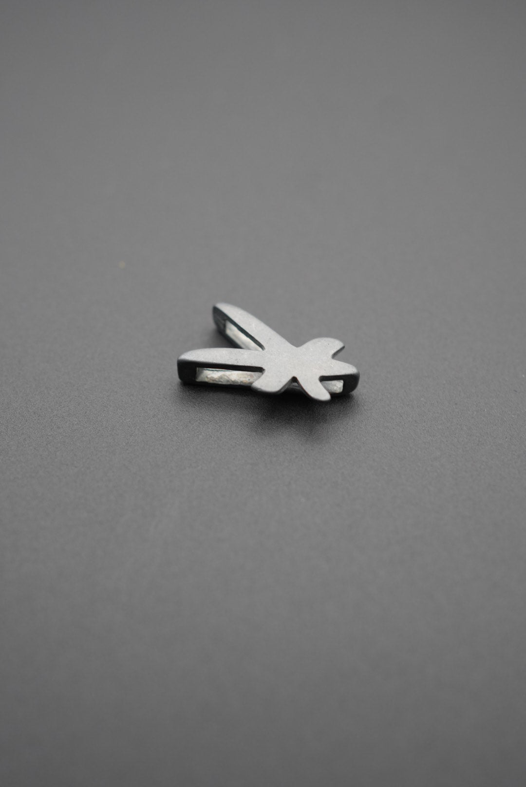 Vista superior del pin metálico libélula sobre superficie gris