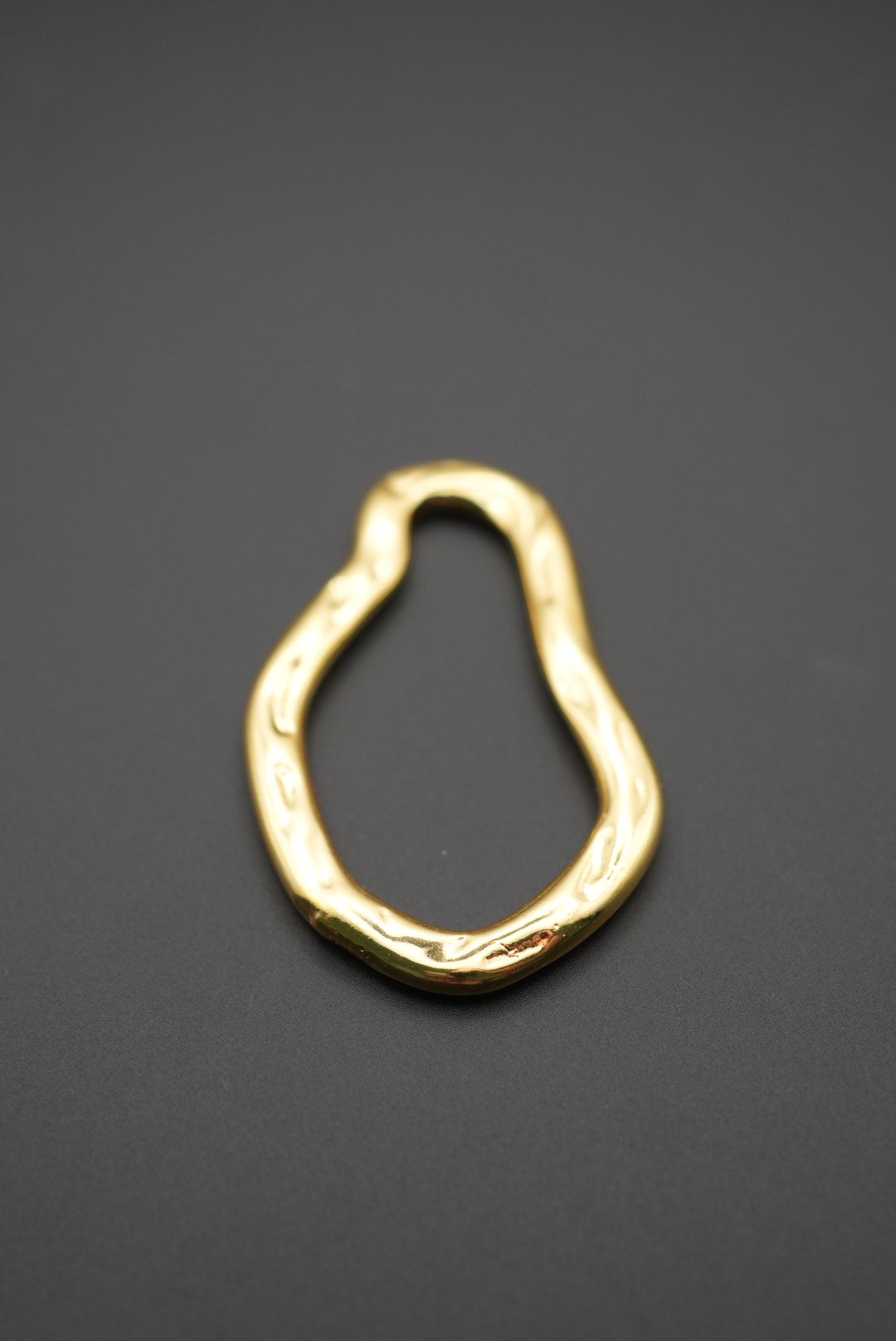 Detalle de pulsera dorada de forma asimétrica sobre fondo oscuro