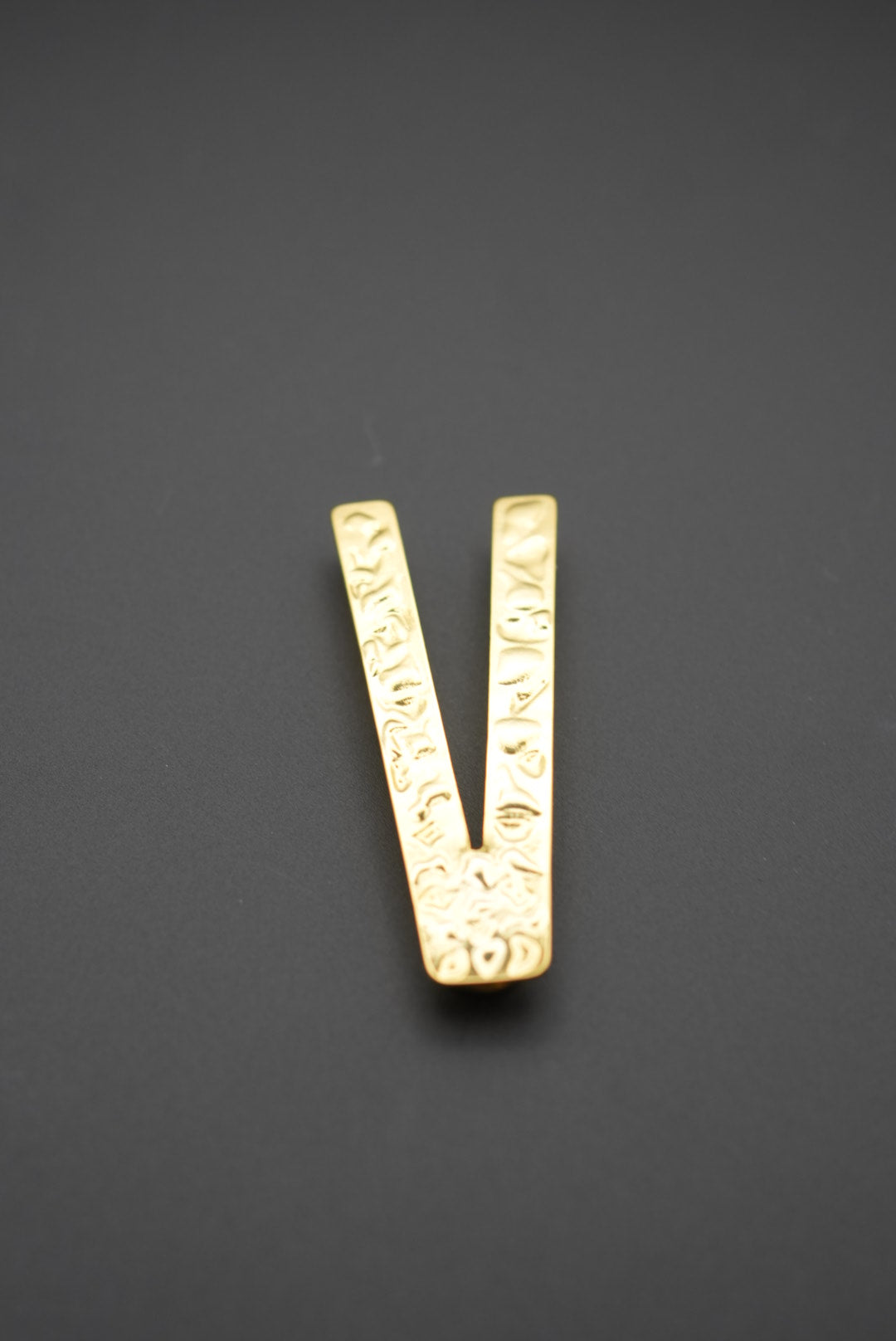 Pinza metálica dorada en forma de V con textura visible en fondo gris