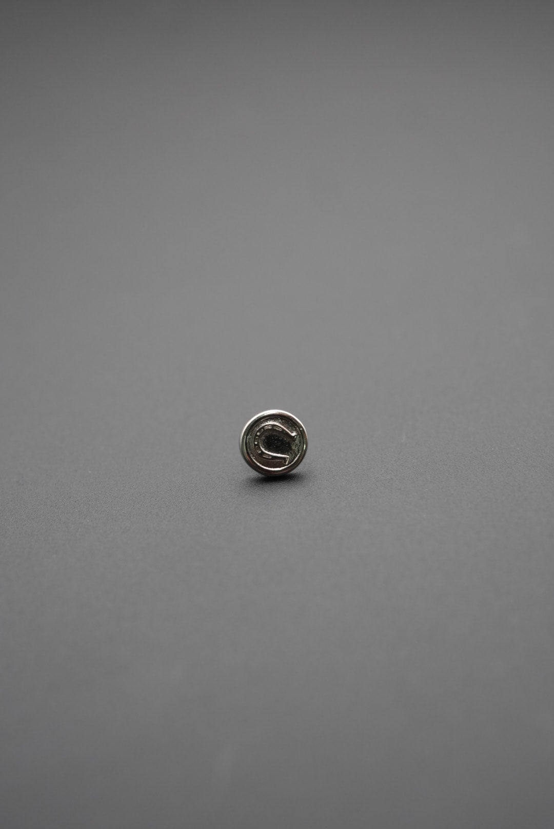 Vista lateral del botón metálico circular con diseño técnico sobre fondo gris