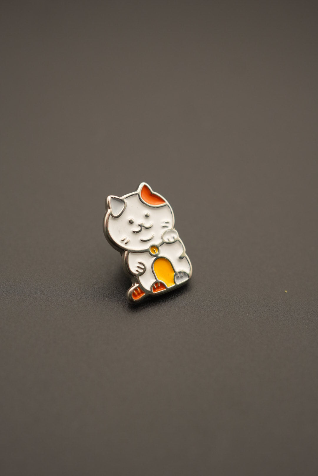 Vista cercana del pin personalizado en forma de gato de la suerte sobre superficie gris