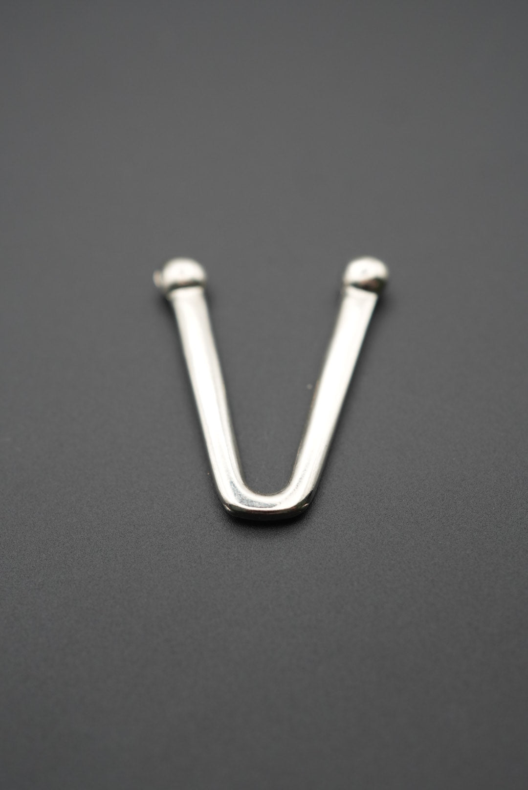 Gancho técnico en V fabricado en metal pulido sobre superficie gris