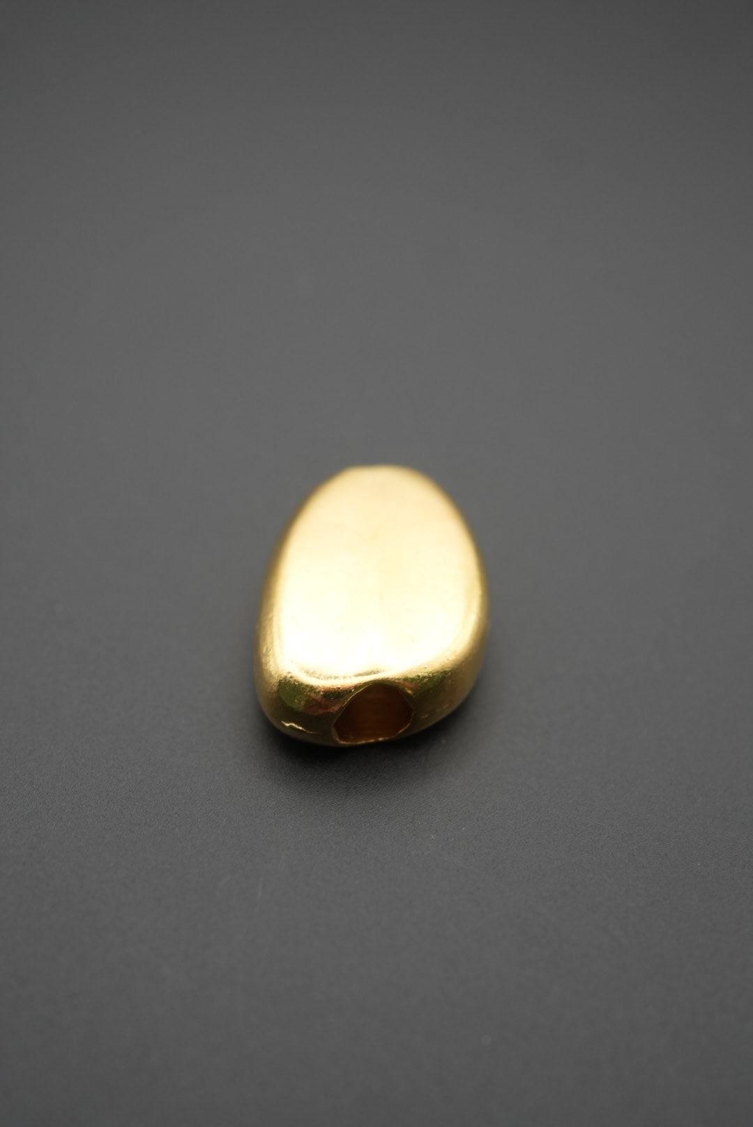 Cuenta ovalada de latón sobre fondo negro resaltando su brillo