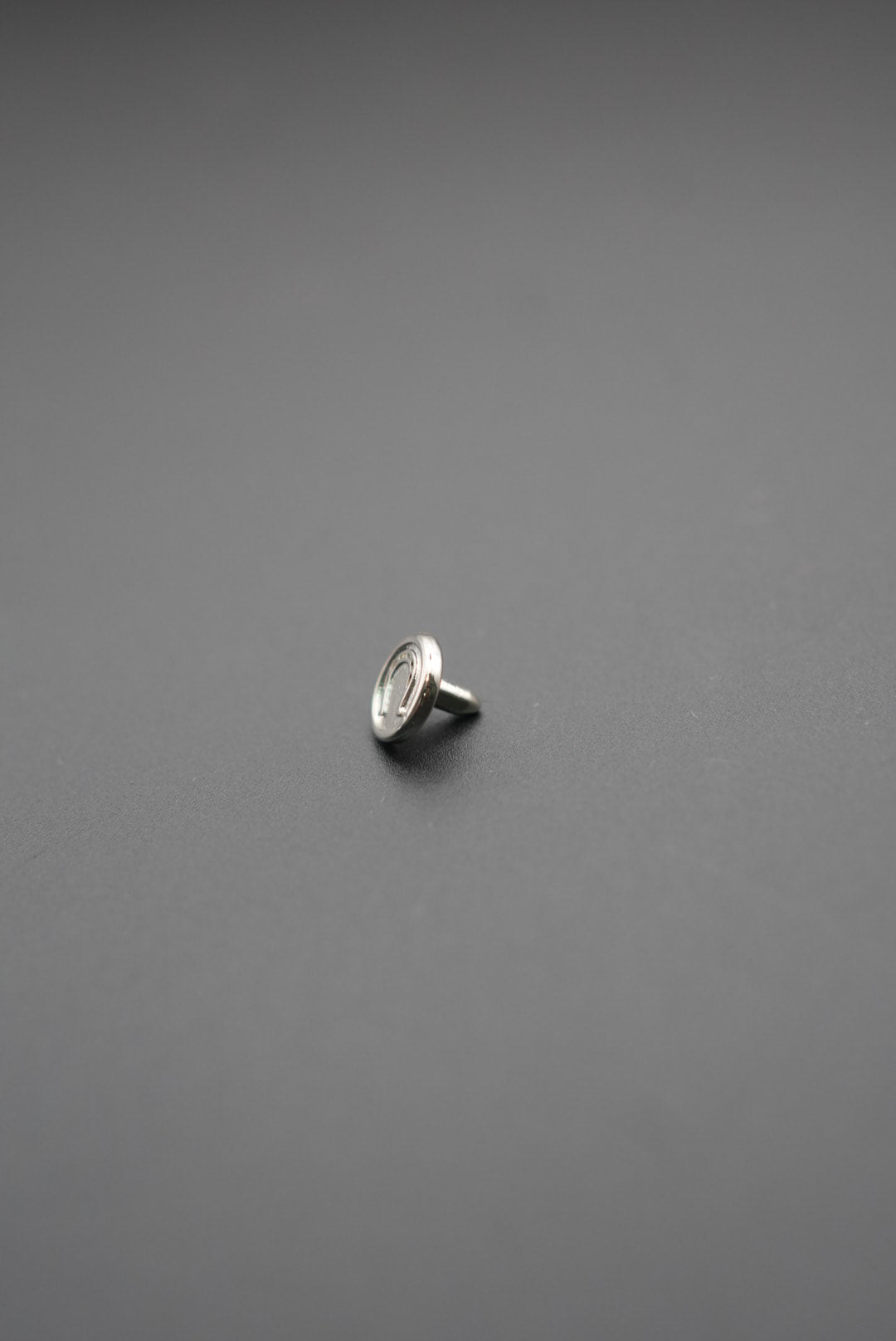 Botón redondo metálico con grabado 'Simon & Simon' en relieve sobre fondo gris