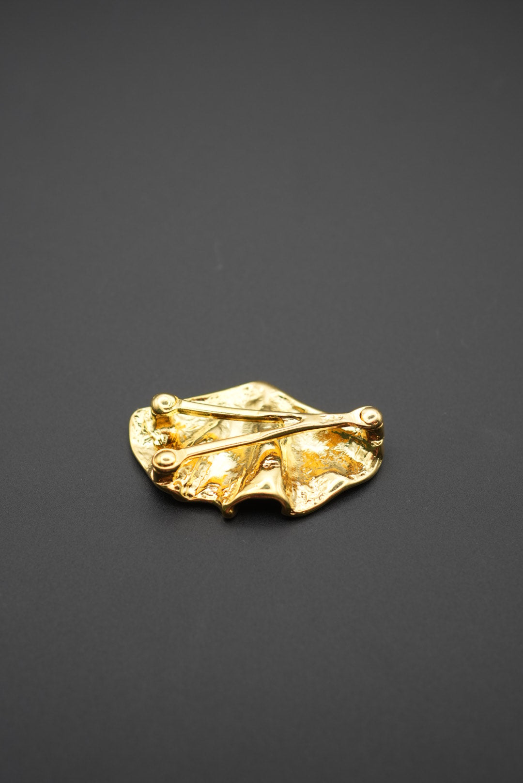 Vista lateral del broche dorado con textura y acabado brillante