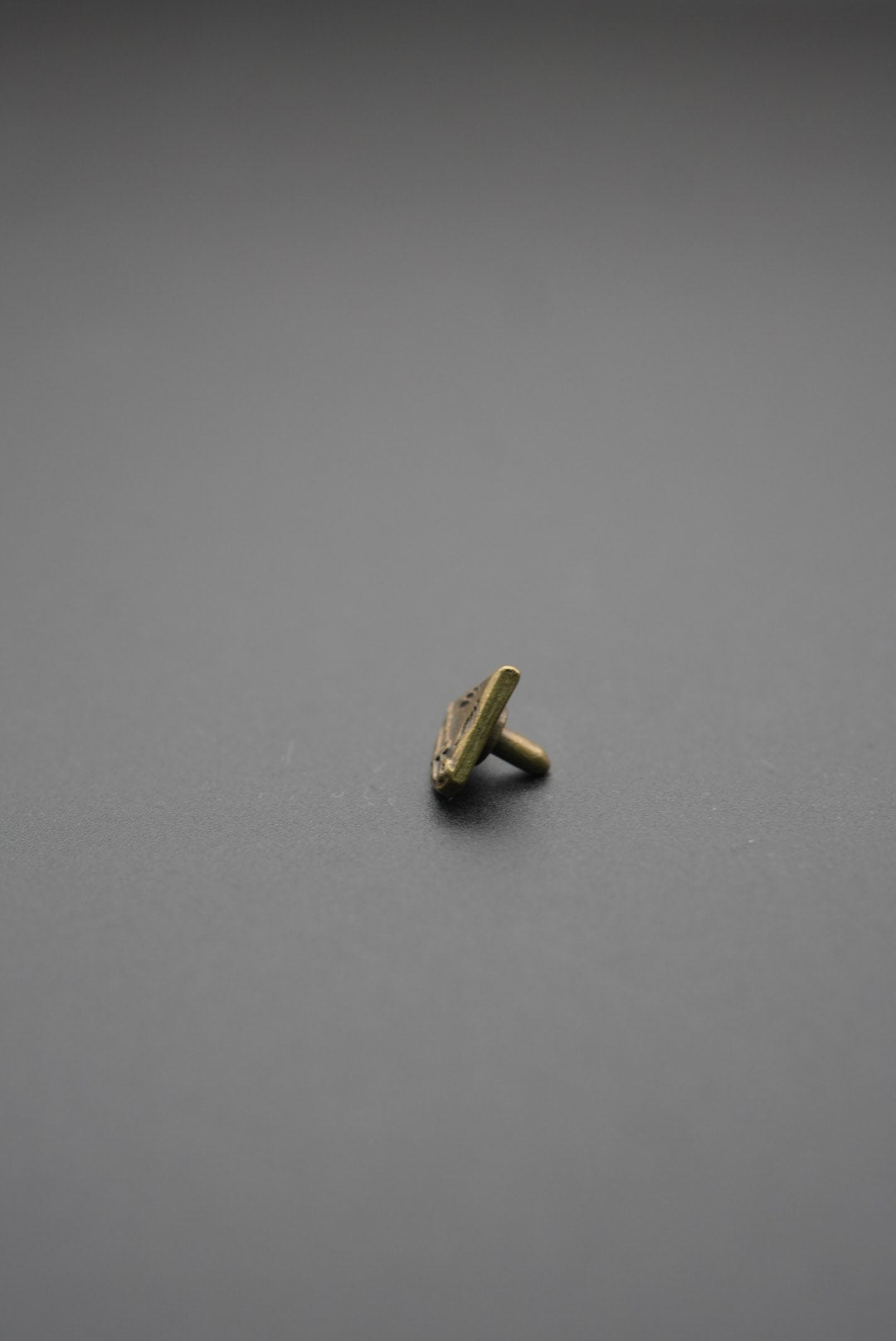 Vista lateral de tachuela metálica triangular mostrando el tornillo