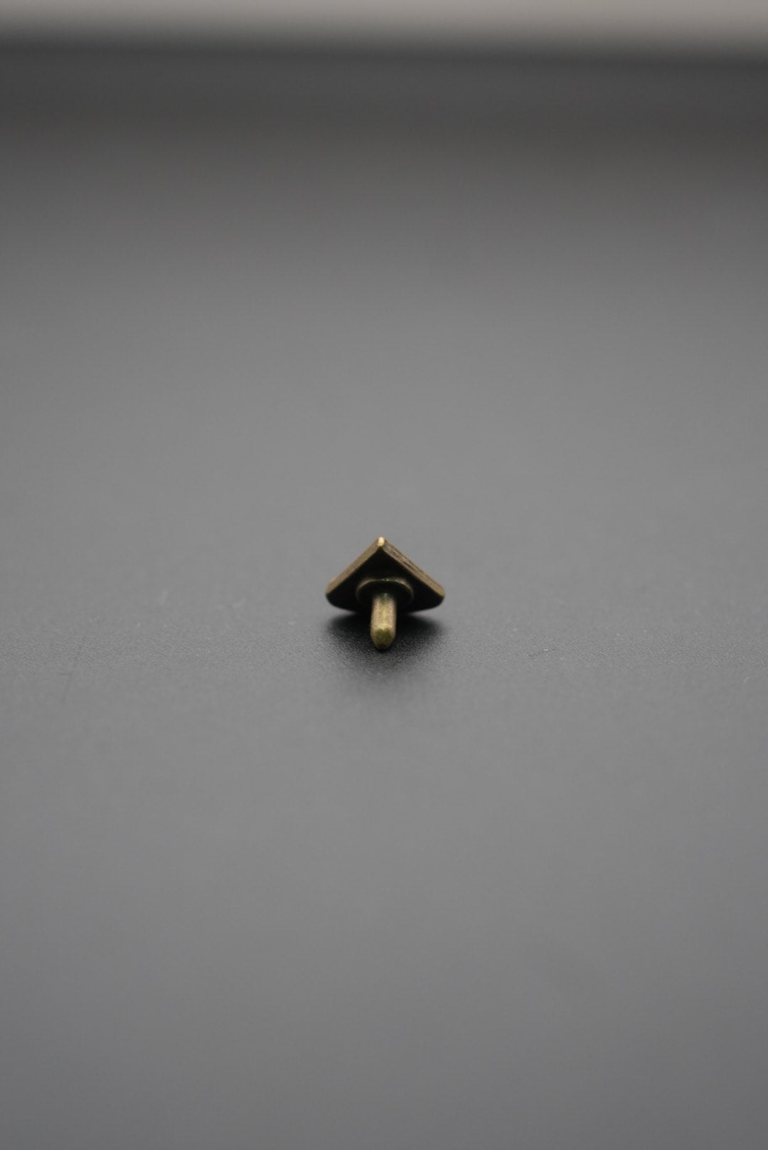 Vista frontal de tachuela metálica triangular con diseño grabado