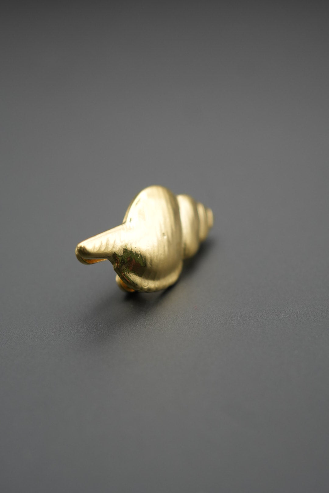 Parte trasera del pin metálico dorado en forma de concha marina con mecanismo de sujeción doble