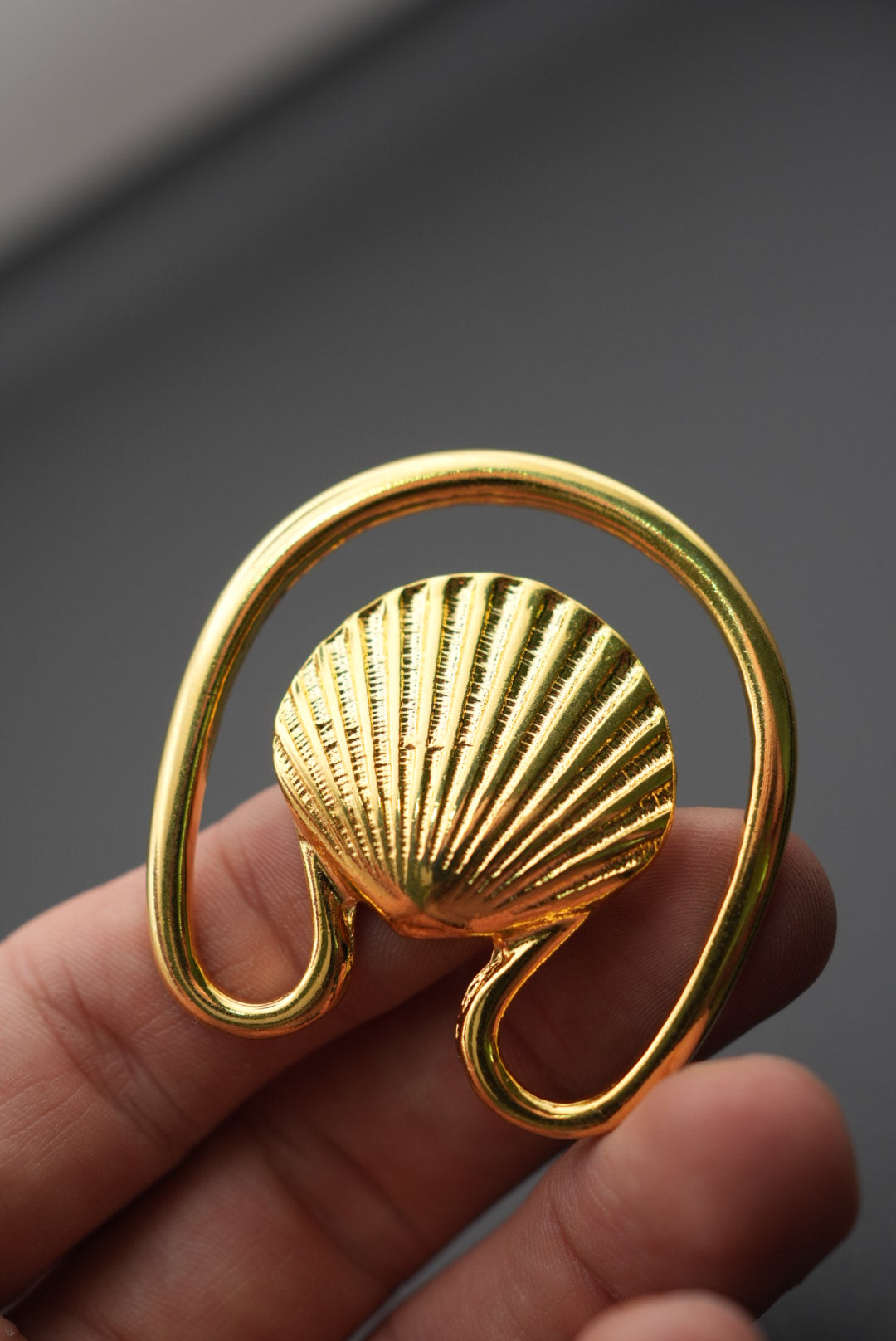 Gancho de metal dorado con forma de concha visto de cerca en mano, fondo oscuro